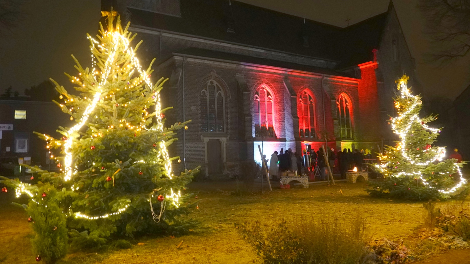 Weihnachtsbäume vor angestrahlter Kirche